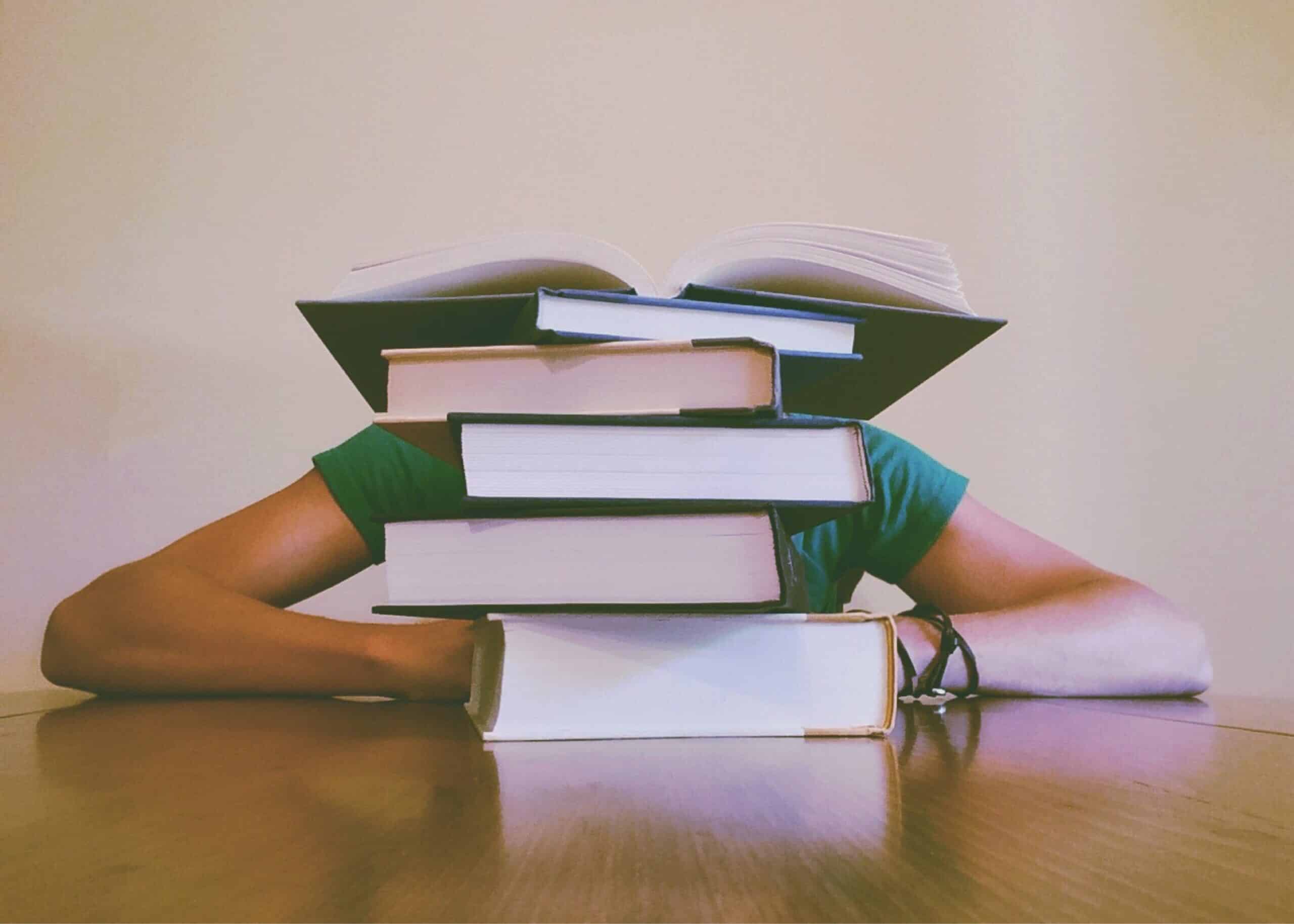 livros empilhados em uma mesa e uma pessoa sentada atras